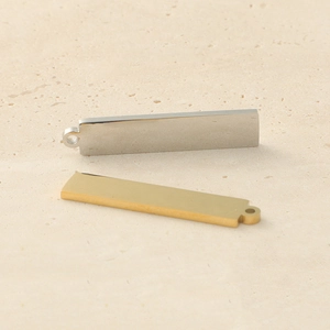Polished gold and silver stainless steel bar pendants on a beige stone surface