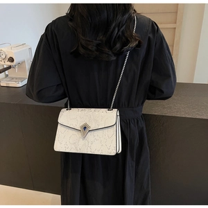 Detail of white snakeskin texture crossbody bag with silver chain and blue gemstone lock