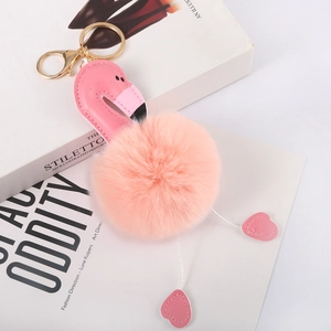 Detailed close-up of pink flamingo fur pompom keychain with golden metal clasp on books