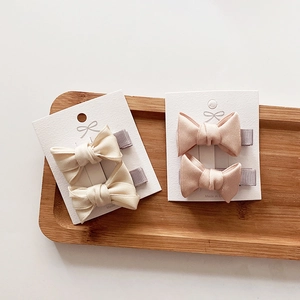 Close-up of fabric bow hair clips in beige and pink displayed on a wooden tray