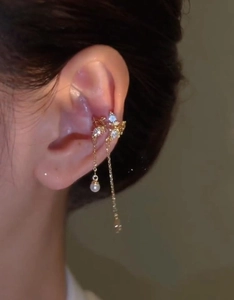 Detailed view of gold tassel ear cuff with bow, star elements and pearl drop on model