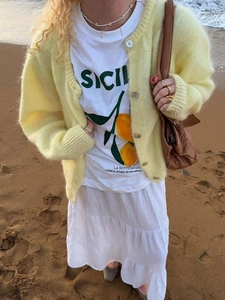 Chic light yellow mohair cardigan paired with white tiered skirt on a beach setting