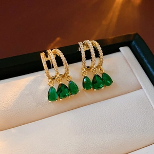 Detailed macro view of gold earrings with drop-shaped green gems in a white jewelry box