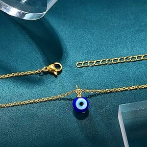 Macro shot of gold stainless steel chain with blue evil eye pendant on a textured surface