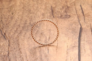 Nahaufnahme eines minimalistischen Roségold-Seilrings auf natürlichem Holzhintergrund