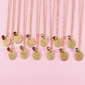 Twelve personalized gold birthstone necklaces with unique floral engravings on a pink background