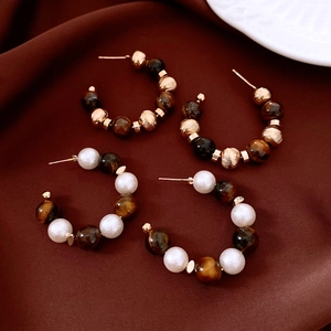 Detail of C-shaped hoop earrings with tiger eye beads and pearls on brown fabric