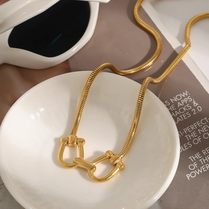 Close-up of gold snake chain necklace with horsebit pendant on white porcelain bowl