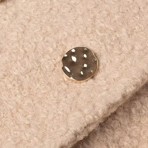 Close-up of curly faux shearling fabric and a textured vintage round metal button