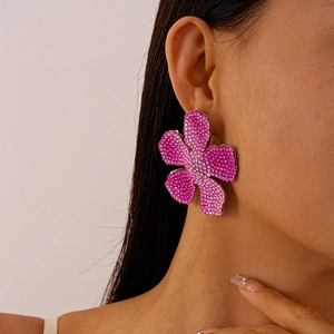 Close-up of model wearing vibrant rose red rhinestone flower earrings with petal details