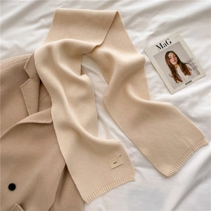 Detail of soft beige knitted scarf texture with stitched emo tag on white fabric
