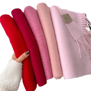 Handheld display of soft wool scarves in a gradient of pink and red shades with tassels