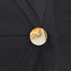 Close-up of black cotton twill baseball cap with decorative yellow textured top button