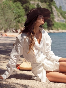 Close-up of a white linen tie-waist shirt dress with a lapel collar on a scenic beach
