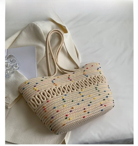 Detail of cream woven tote bag with colorful pom-poms and wavy textured weave patterns