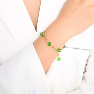 Detail of double-layer gold snake chain bracelet with green glass beads on model wrist