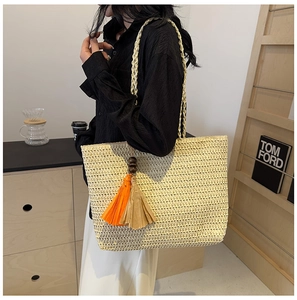 Detail of hand-woven straw tote bag with colorful orange tassels and decorative wood beads