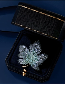 Macro shot of maple leaf brooch with green and blue crystals in a black velvet jewelry box