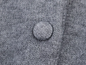 Gros plan sur la texture d'un tricot gris avec un bouton recouvert de tissu décoratif