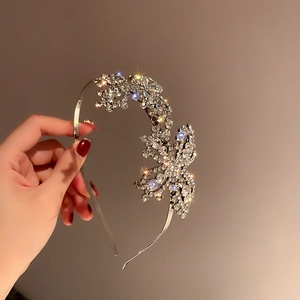 Gros plan d'un serre-tête papillon en strass argentés brillants tenu devant un mur uni