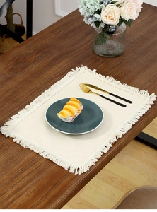 Detail of cream white linen placemat with fringe on a dark wooden dining table