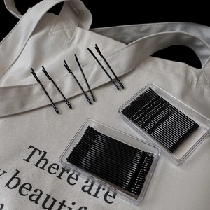 Minimalist black wave bobby pins set in clear storage box on a white canvas bag