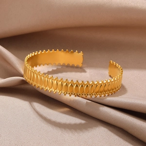 Detail of gold open bangle with embossed oval patterns and fine beaded edges on silk