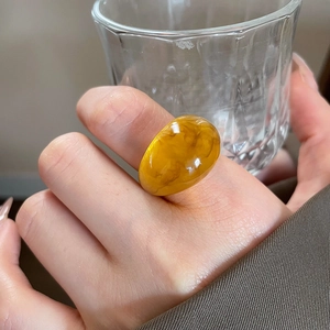 Macro view of amber resin ring with marble texture on hand holding a glass cup