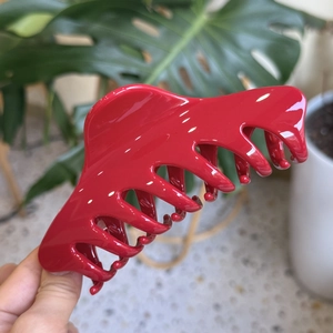 Large red acrylic hair claw clip with high-gloss finish held against a soft natural background