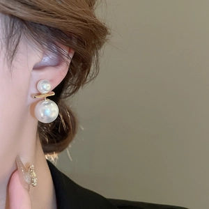 Close-up of minimalist gold earring with two pearls worn by a model in a profile view