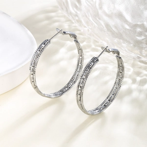 Macro detail of large silver chain textured hoop earrings with sparkling diamond-cut finish