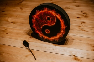 Detail of Shamanic drum with flame Tai Chi pattern on light wood floor with drumstick