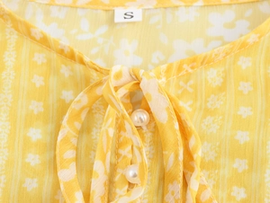 Detail of floral chiffon dress neckline with dainty pearl buttons and a tie closure