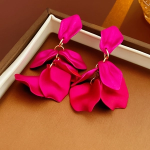 Détails de boucles d'oreilles à pétales fuchsia avec chaîne dorée sur plateau élégant