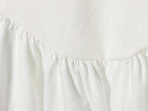 Close-up of white pleated batwing dress fabric showing detailed stitching and texture