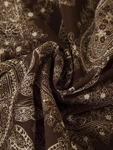 Gros plan du motif paisley sur un tissu en mousseline plissée marron foncé souple