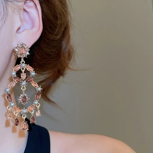 Detail of elegant gold-plated earrings with pink teardrop gems and pearls on a model
