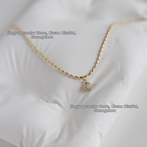 Detailed view of round light blue stone pendant on a delicate 18K gold-plated chain