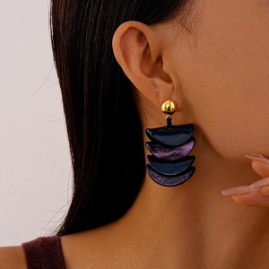 Detail of blue and purple resin crescent earrings with gold studs on a model