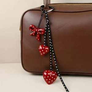 Detail of red heart and bow charms on a polka dot ribbon attached to a brown leather handbag