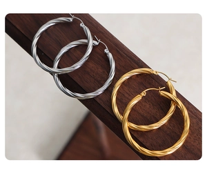 Detailed view of twisted gold and silver hoop earrings on a dark wood surface