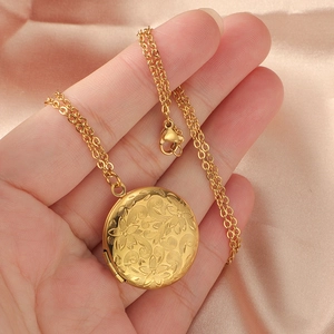 Détail d'un médaillon doré gravé de fleurs tenu à la main sur du satin rose doux