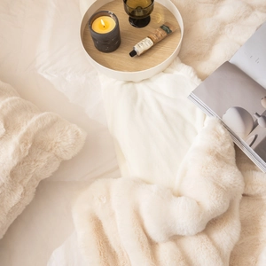 Detail of soft cream white faux rabbit fur throw blanket with cozy home decor and candles