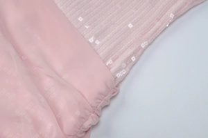 Detailaufnahme von rosa Pailletten-Netzgewebe und Plisseenähten an einem figurbetonten Kleid