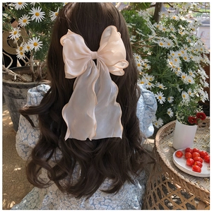 Detail of a beige organza oversized bow hair clip worn in a sunny outdoor garden setting