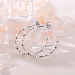 Detailed close-up of C-shaped silver pearl hoop earrings on decorative ice cubes