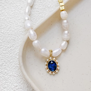 18k gold plated pearl necklace with large blue oval pendant and smiley charm on ceramic tray