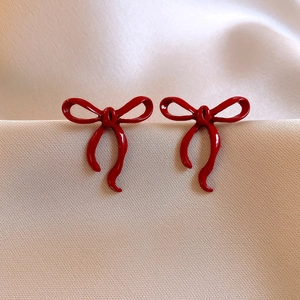 Detailed view of red bow knot stud earrings with a glossy lacquer finish on silk