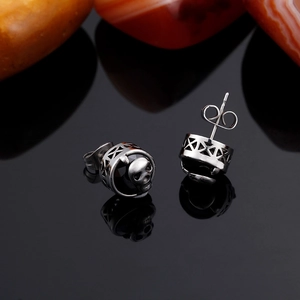 Macro shot of punk style stainless steel skull earrings with black stones on black glass