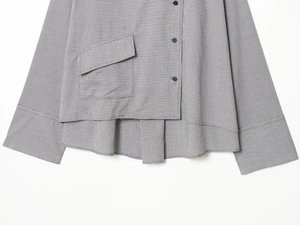 Detail of grey checkered shirt featuring dark buttons, oversized pocket and irregular hem